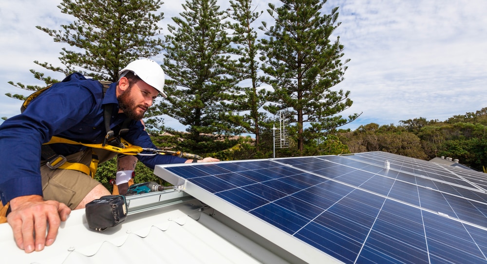 Technician installing rooftop solar panels with safety harness