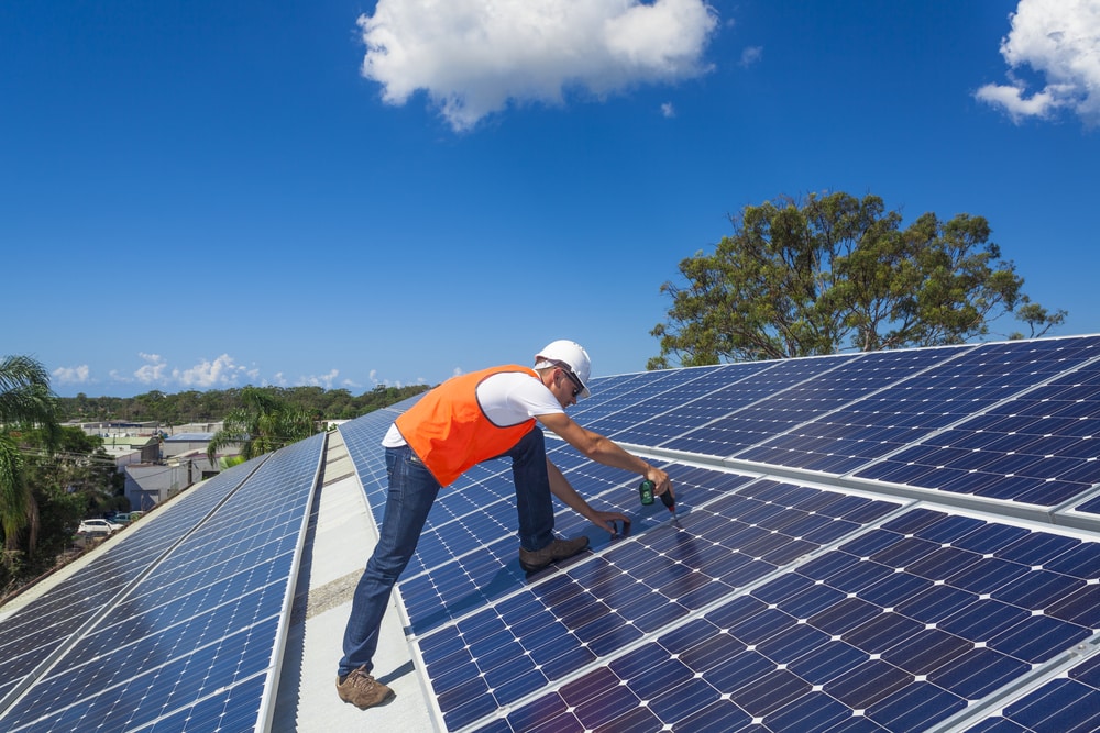 Technician installing rooftop solar panels under blue sky