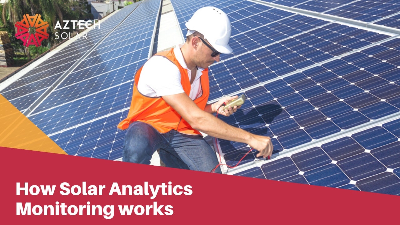 Technician in hi-vis kneeling on rooftop solar panels testing monitoring equipment